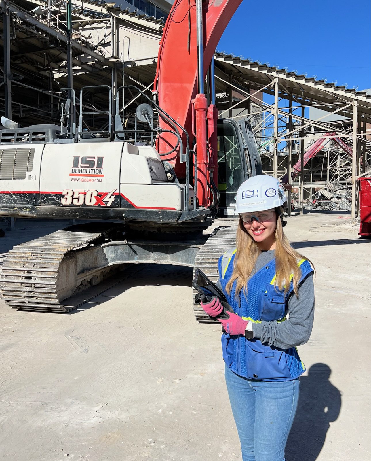 Female construction worker standing with a clipboard in front of an excavator