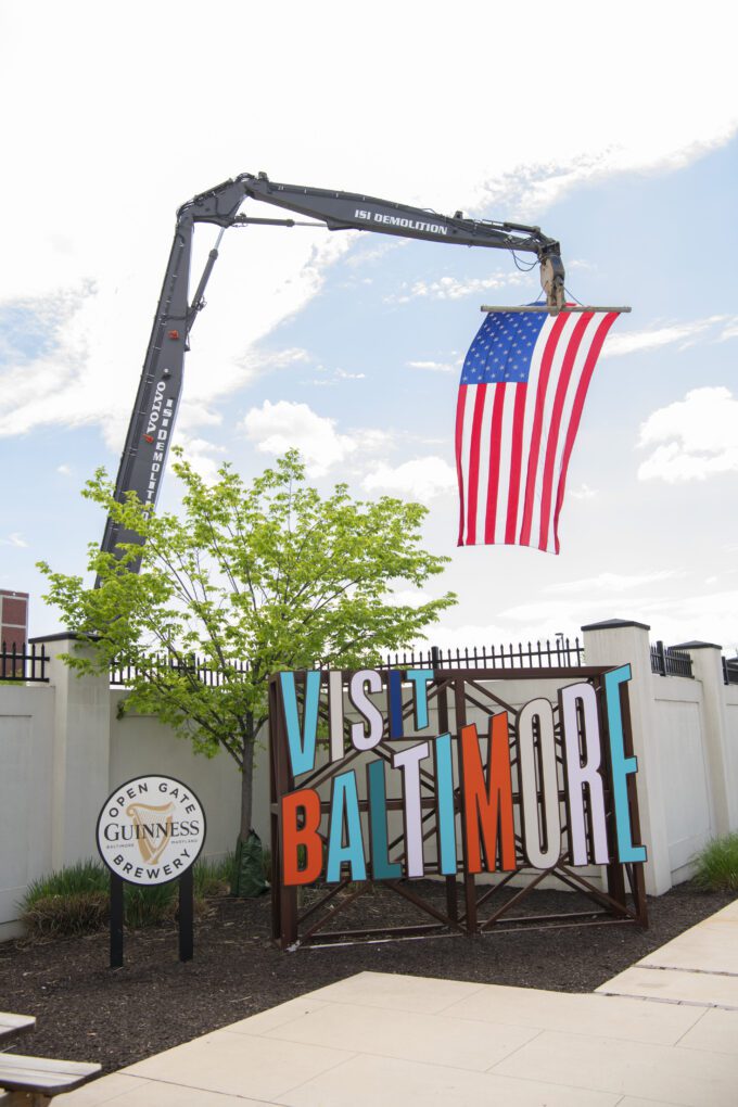 Large American flag hanging from ISI Demolition high reach excavator above Visit Baltimore and Guinness signs